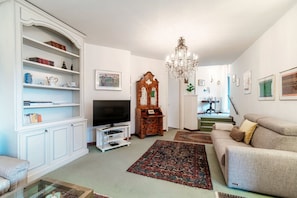 Ein Wohnzimmer mit Fernseher, einer Chandelüster, einer Couch und einem Bücherregal.