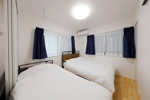 Une petite chambre propre, avec deux lits simples, une fenêtre avec des rideaux et un appareil de climatisation.