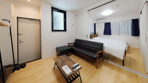 Moderni hotellihuone, jossa on suuri sänky, musta nahkasohva, puinen sohvapöytä ja peili, joka heijastaa huonetta.