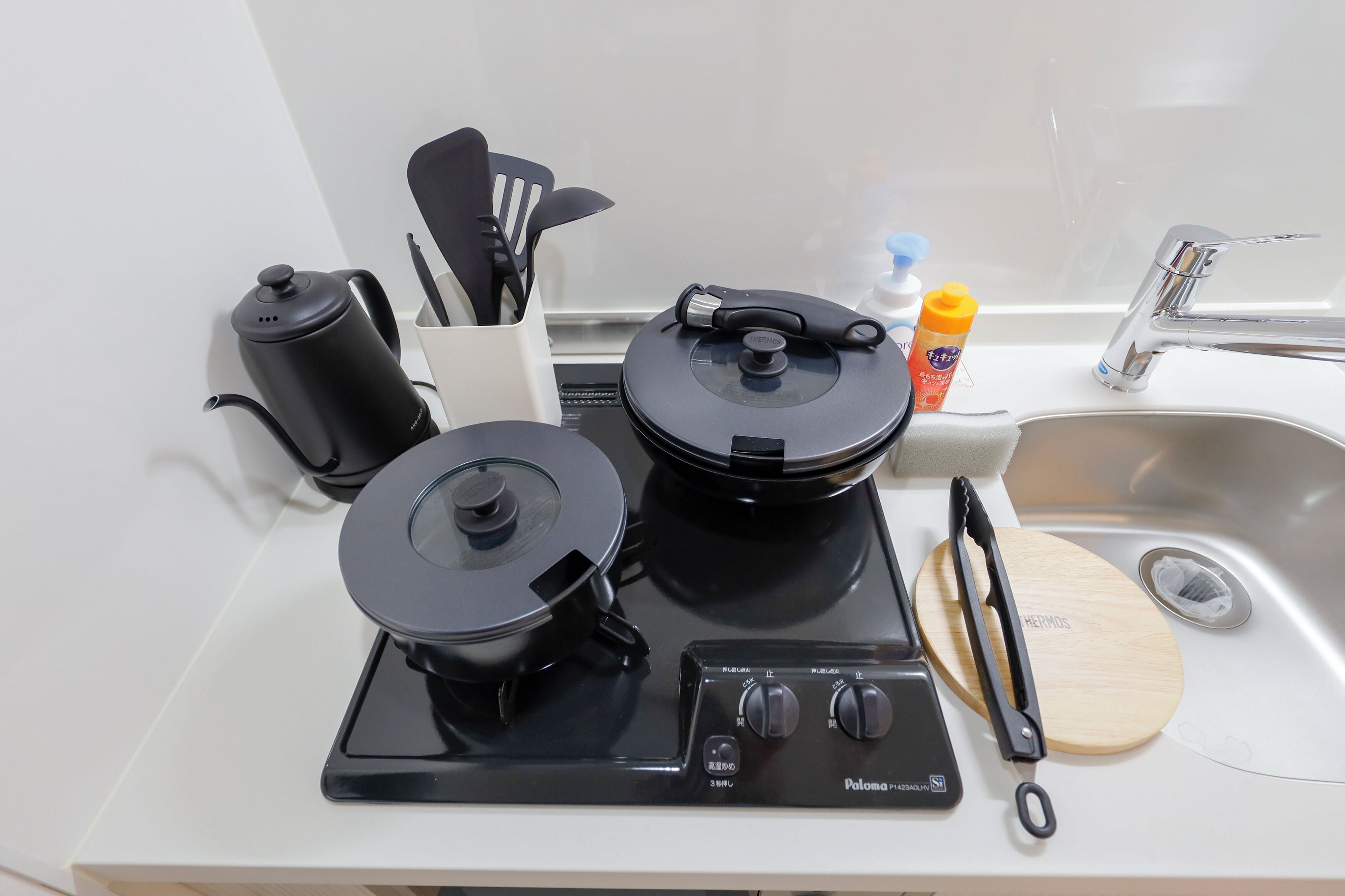 Een keuken met een fornuis, waterkoker en spoelbak.