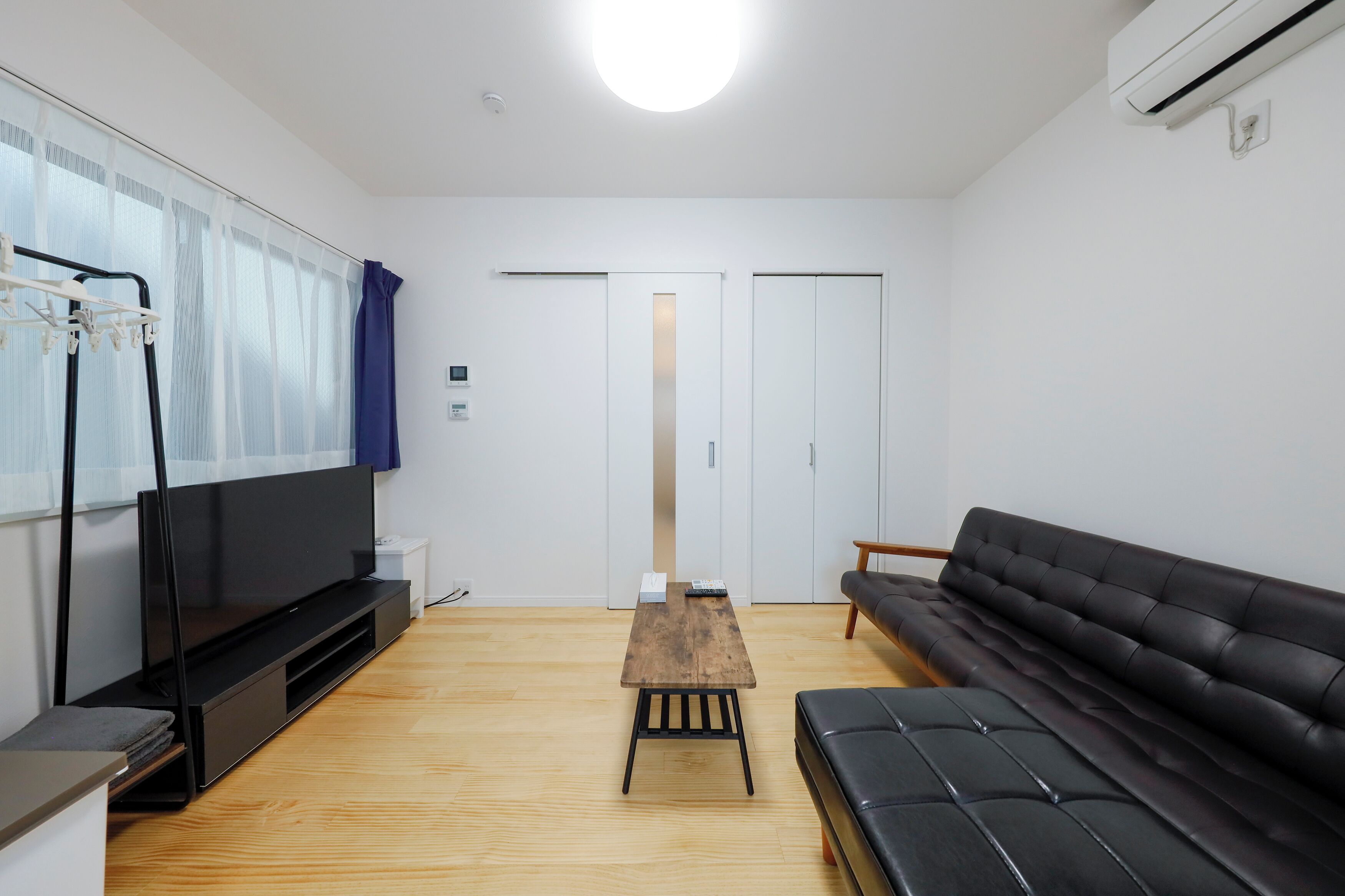 A modern living room with a flat-screen TV, a wooden coffee table, a black leather sofa, and a sliding door closet.