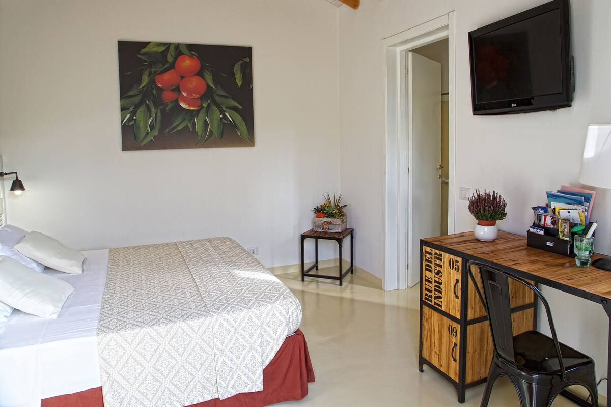 Une chambre à coucher avec un lit, un bureau avec une chaise, une télévision et un tableau accroché au mur.