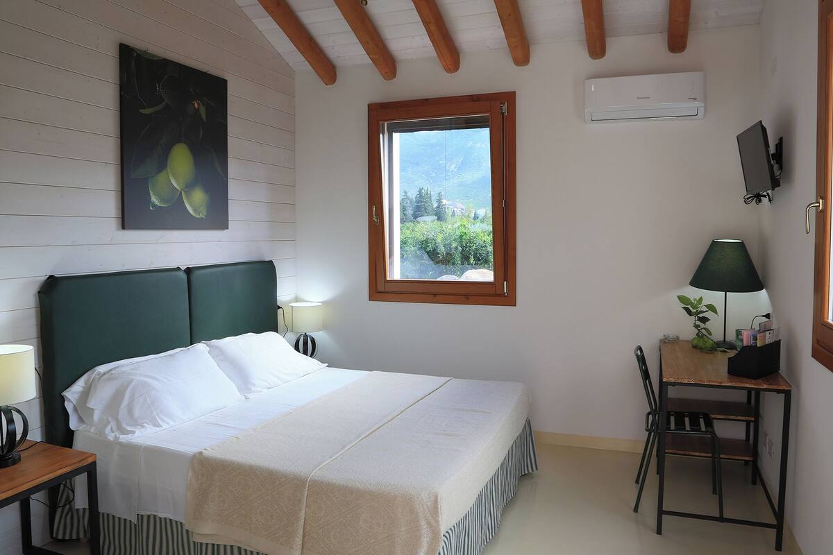 Une chambre à coucher avec un lit, un bureau, une chaise, une fenêtre et un tableau accroché au mur.
