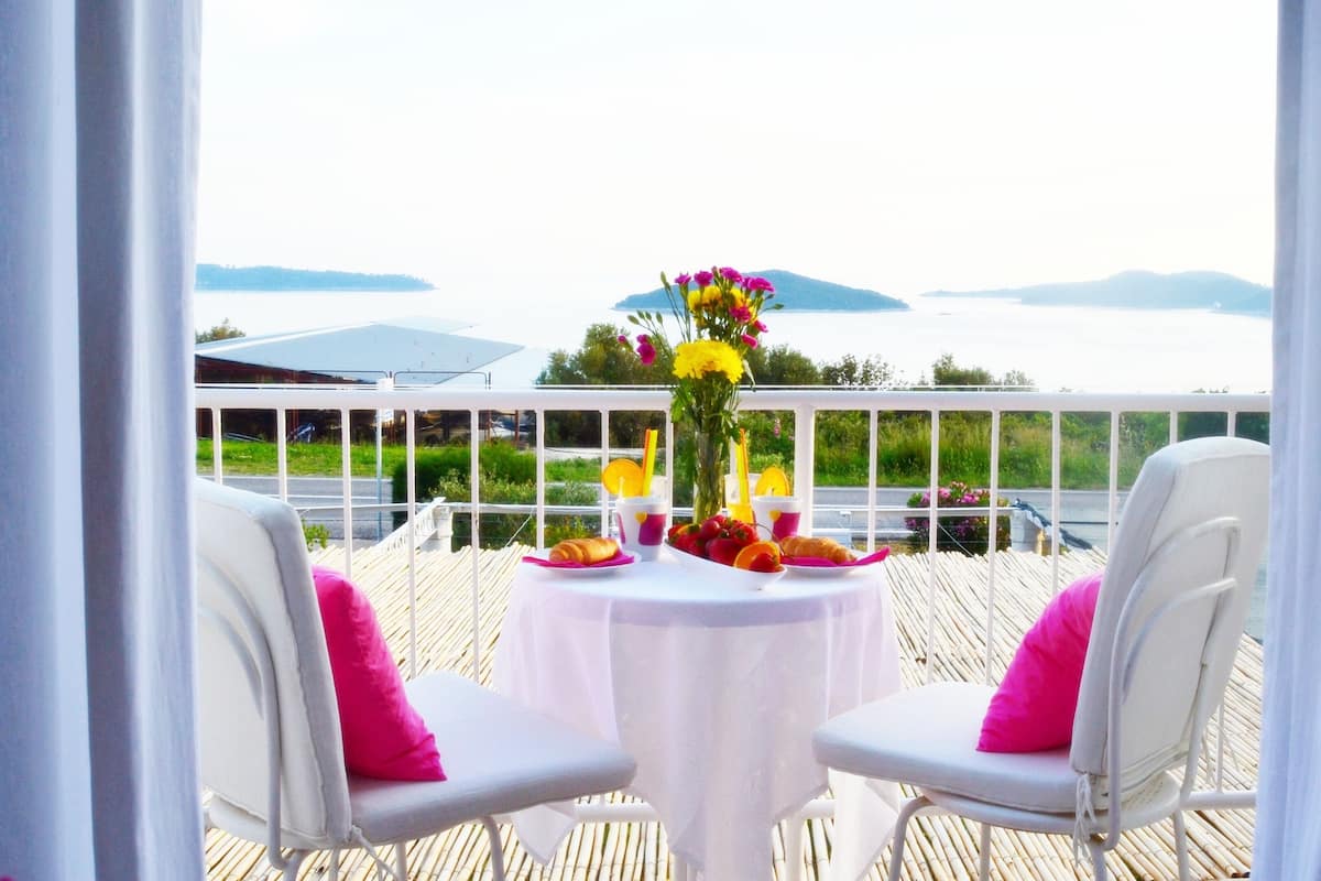 A table with a white tablecloth, two white chairs with pink cushions, and a vase of flowers.