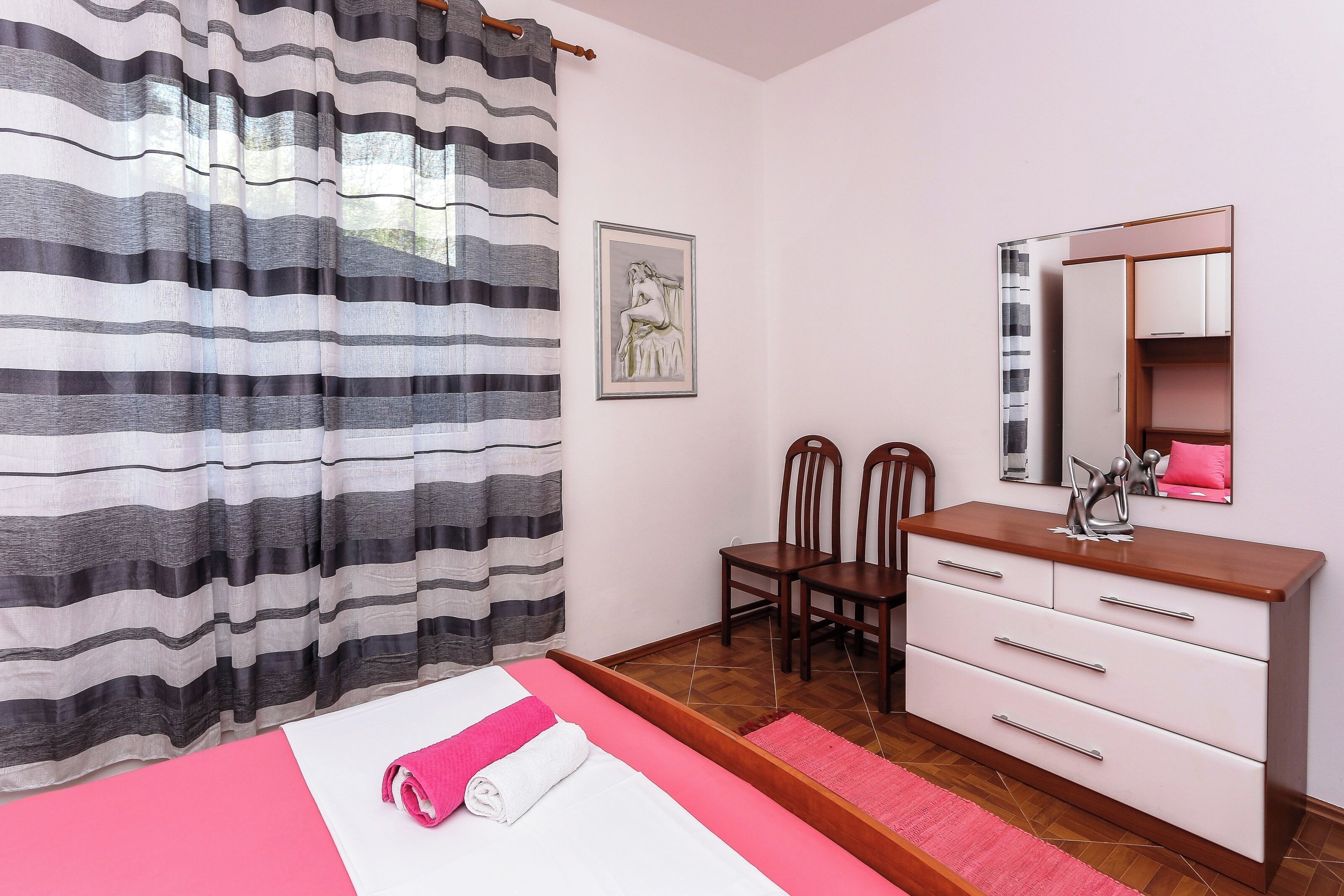 A bedroom with a bed, a wooden dresser, a mirror, and a framed picture on the wall.
