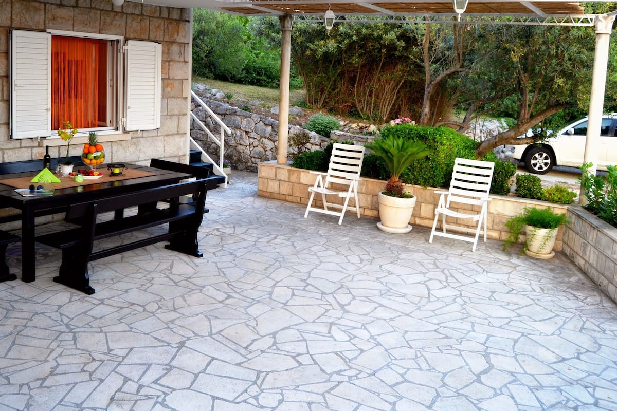 A stone patio with a pool table, outdoor seating, and a stone wall.