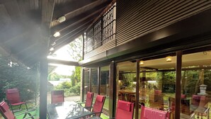 An outdoor dining area with glass walls, red chairs, and a glass table. - Best of Ilidza Villa (Sarajevo)