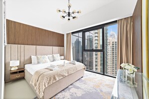Een moderne slaapkamer met een groot bed, een nachtkastje, een glazen tafel en uitzicht op hoge gebouwen.