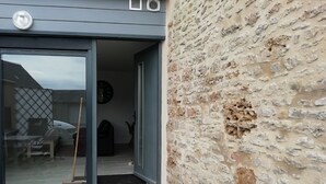 A building entrance with a glass door, a clock, and a stone wall. - G2 LA Cour à Proximité de la Plage de Ravenoville Plage (Sainte-Mère-Église)