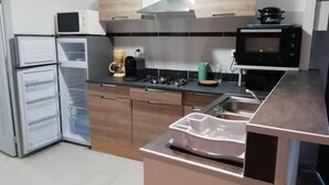 A modern kitchen with a built-in oven, microwave, and stove. There is a coffee maker and a kettle on the counter. - G2 LA Cour à Proximité de la Plage de Ravenoville Plage (Sainte-Mère-Église)