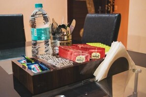 Een tafel met een waterfles, een bakje bestek en porties snacks.