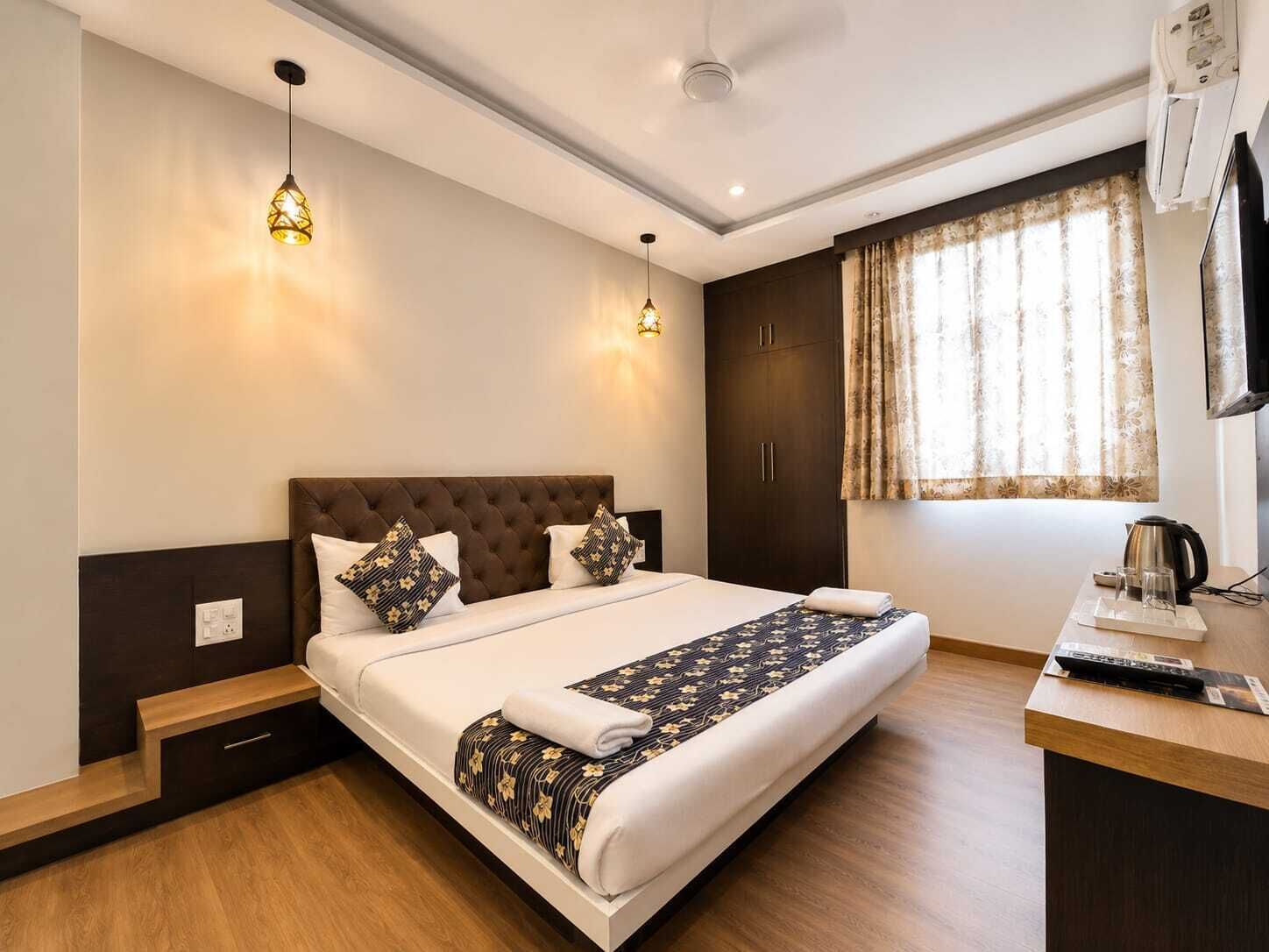 A hotel room with a large bed, bedside tables, a desk with a kettle, and a window with curtains.