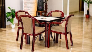 Un coin repas avec une table en bois et quatre chaises, une plante en pot et un escalier en arrière-plan.