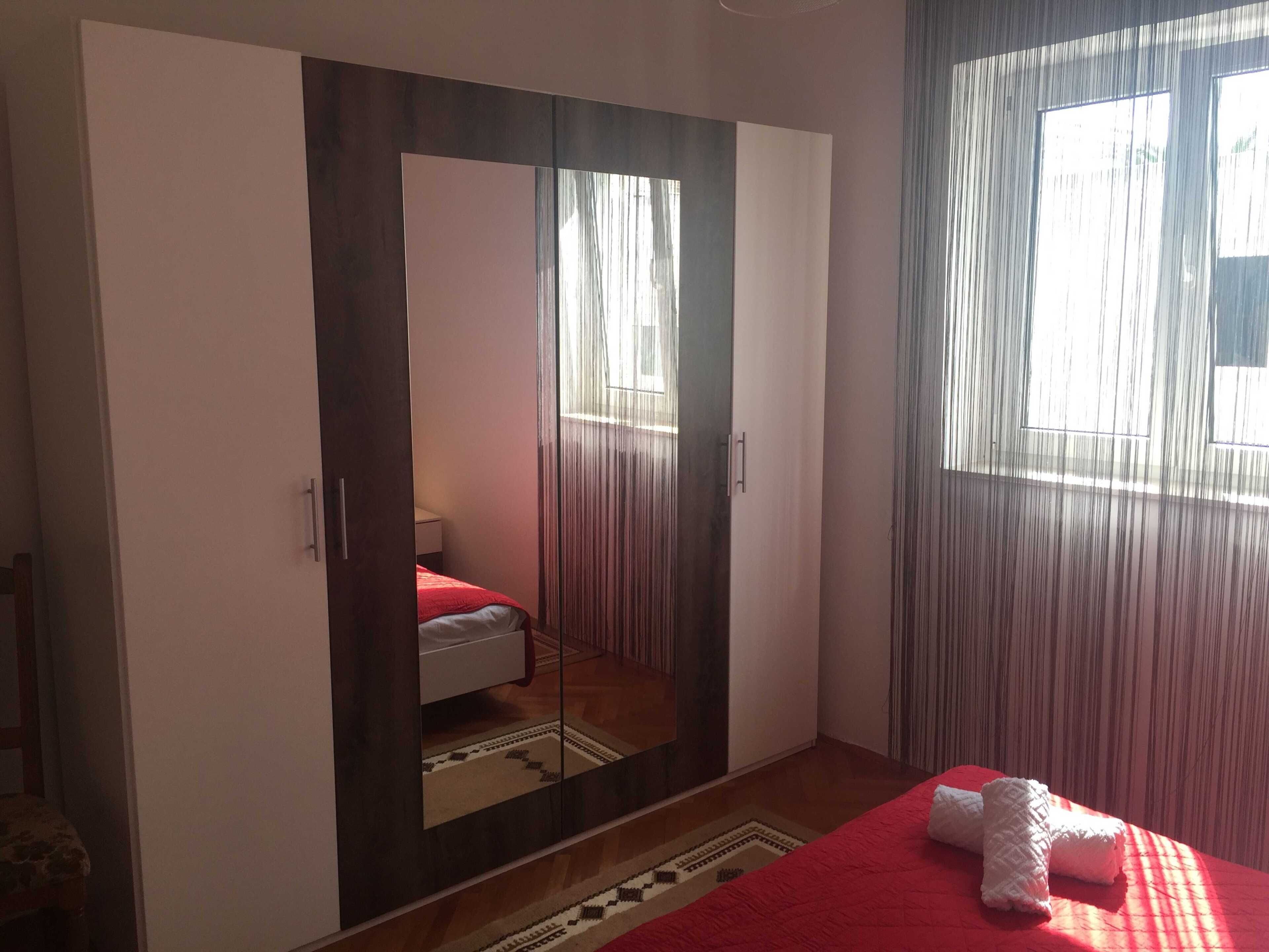 Ein Schlafzimmer mit großem Kleiderschrank, einem Bett mit roter Bettdecke und einem Fenster mit Vorhängen.