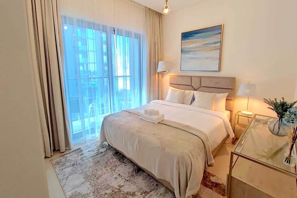 A hotel room with a large bed, a glass coffee table, a painting on the wall, and a view of the city through the window.