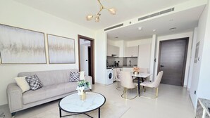 Een moderne woonkamer met een bank, salontafel en stoelen, een keuken met een eettafel, en een grote deur die leidt naar een andere kamer.