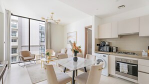 A modern kitchen with a dining area, a washing machine, and a large window with curtains. - Sobha Creek Vista Tower A Apartments (Dubai)