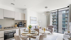 A modern kitchen with a gas stove, oven, and microwave. There is a dining area with a round table and chairs. The room has large windows with a view of high-rise buildings. - Sobha Creek Vista Tower A Apartments (Dubai)