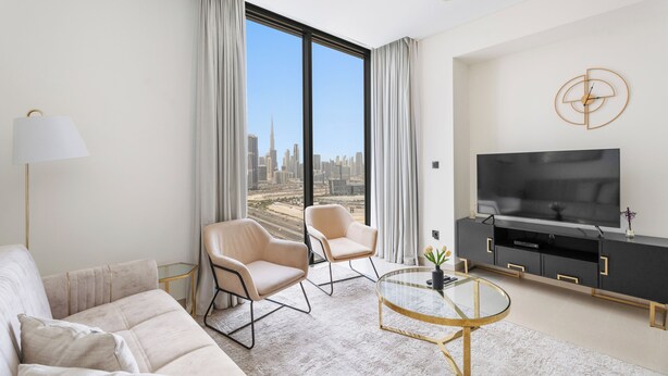 A modern hotel room with a large window offering a city view, a sofa, two armchairs, a glass coffee table, a TV, and a minimalist decor. - Sobha Creek Vista Tower A Apartments (Dubai)