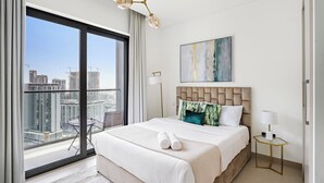 A modern hotel room with a large balcony, a bed with white linens, a gold-framed nightstand, and a contemporary chandelier. - Sobha Creek Vista Tower A Apartments (Dubai)
