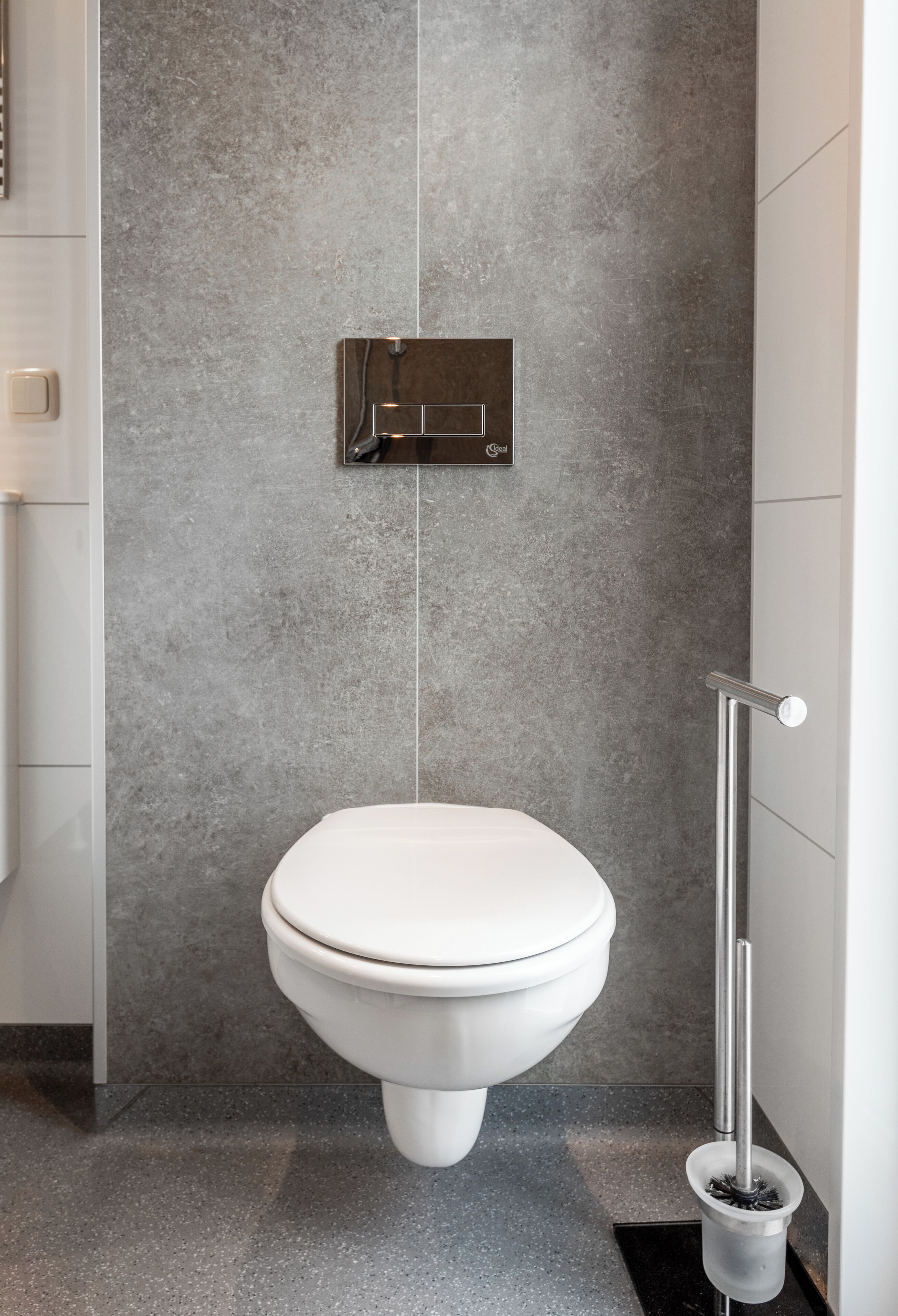 A modern bathroom with a white toilet, a wall-mounted flush handle, and a floor-mounted bidet.