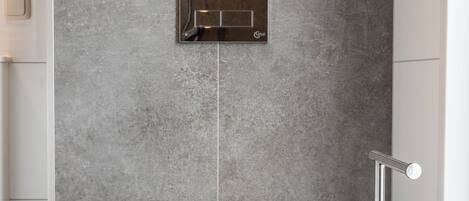 A modern bathroom with a white toilet, a wall-mounted flush handle, and a floor-mounted bidet.