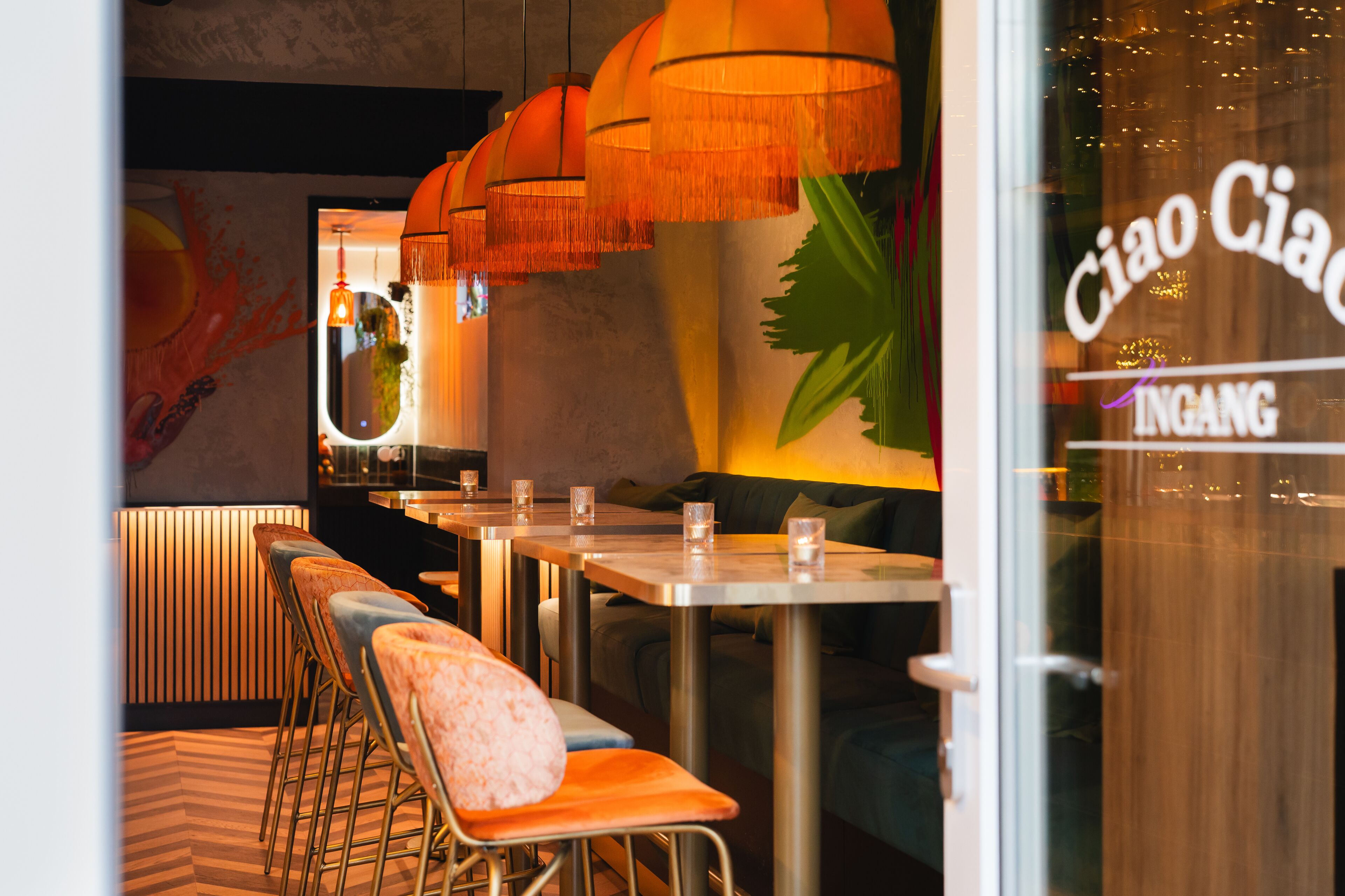 A restaurant interior with booths, hanging orange lamps, and a wall with a plant.