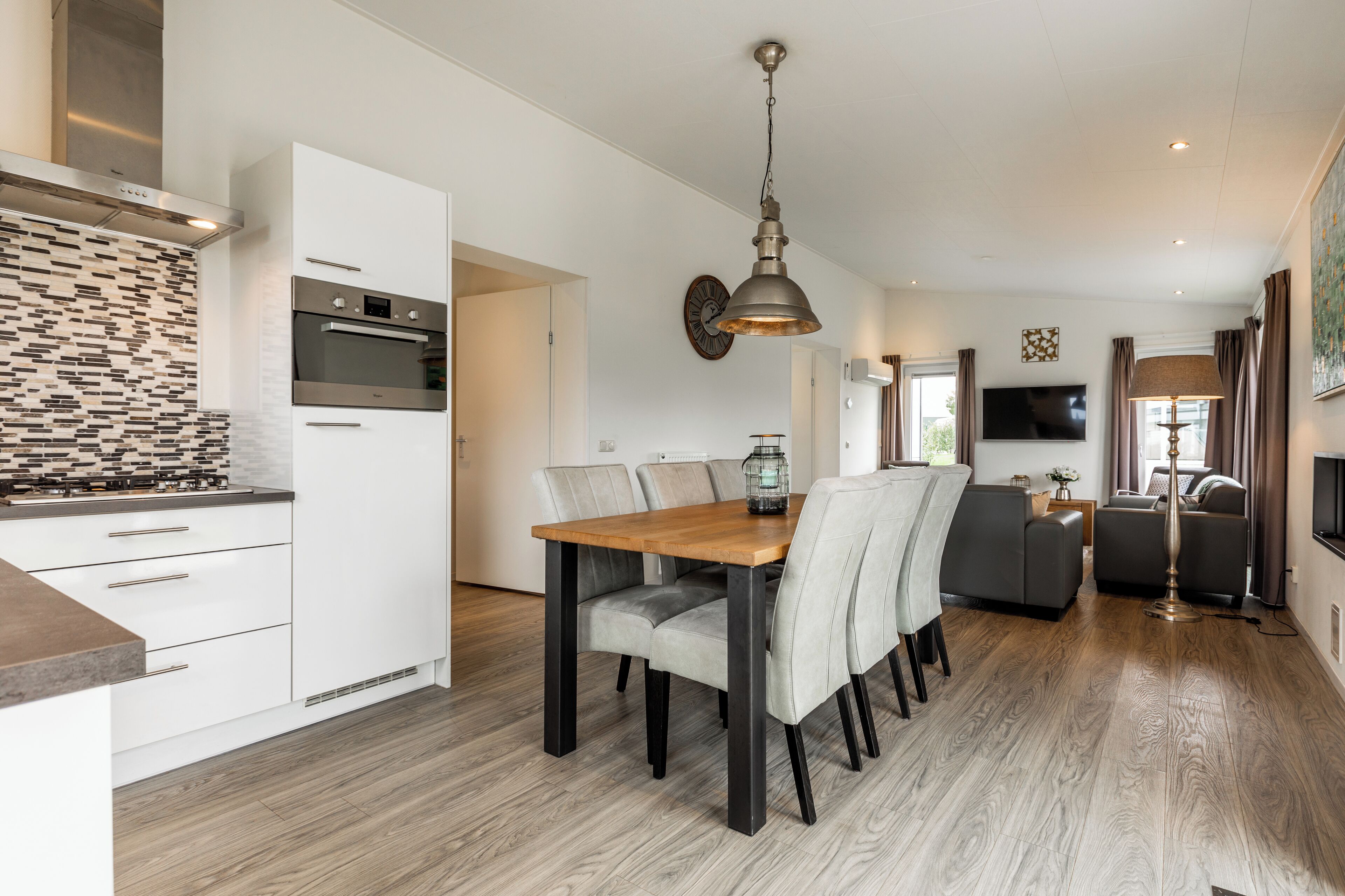 Een moderne keuken met witte kasten, een inbouwoven en een betegelde spatwand.