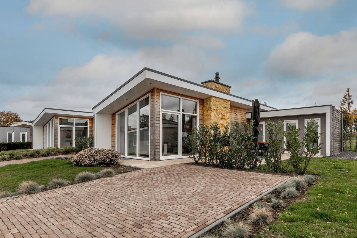 A modern house with a brick pathway leading to a glass door entrance, surrounded by well-maintained lawns and shrubs.