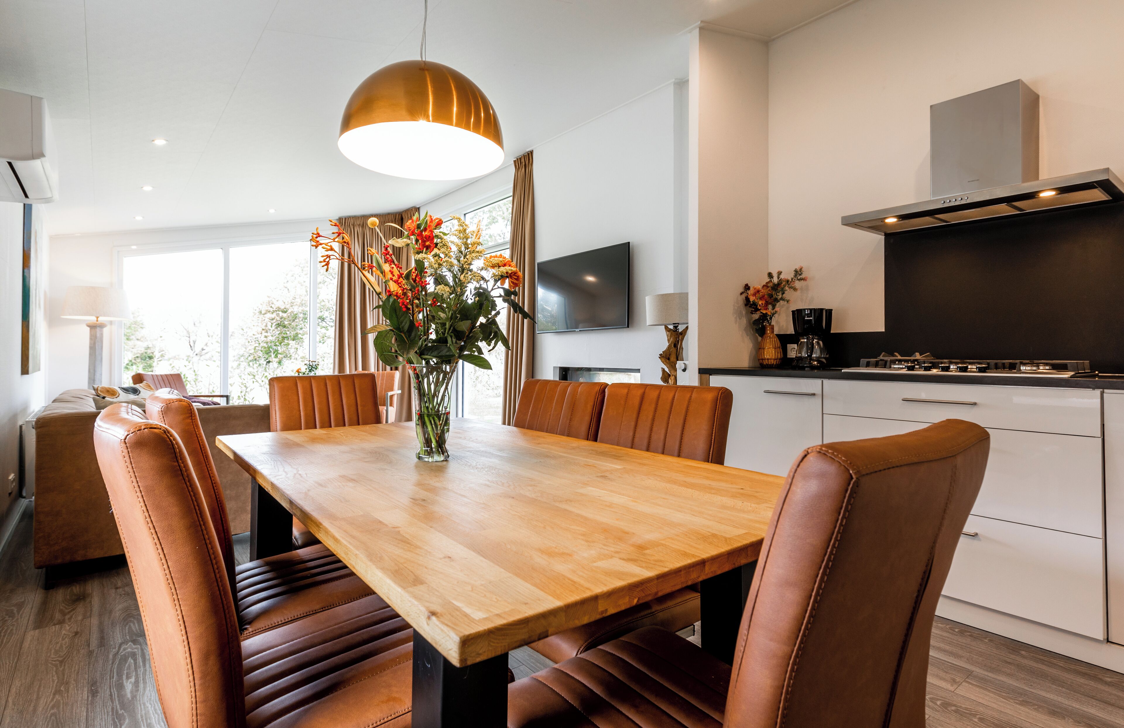 Ein stilvoller Essbereich mit einem Holztisch, Ledersesseln, einem Blumenstrauß und einer großen Pendelleuchte.