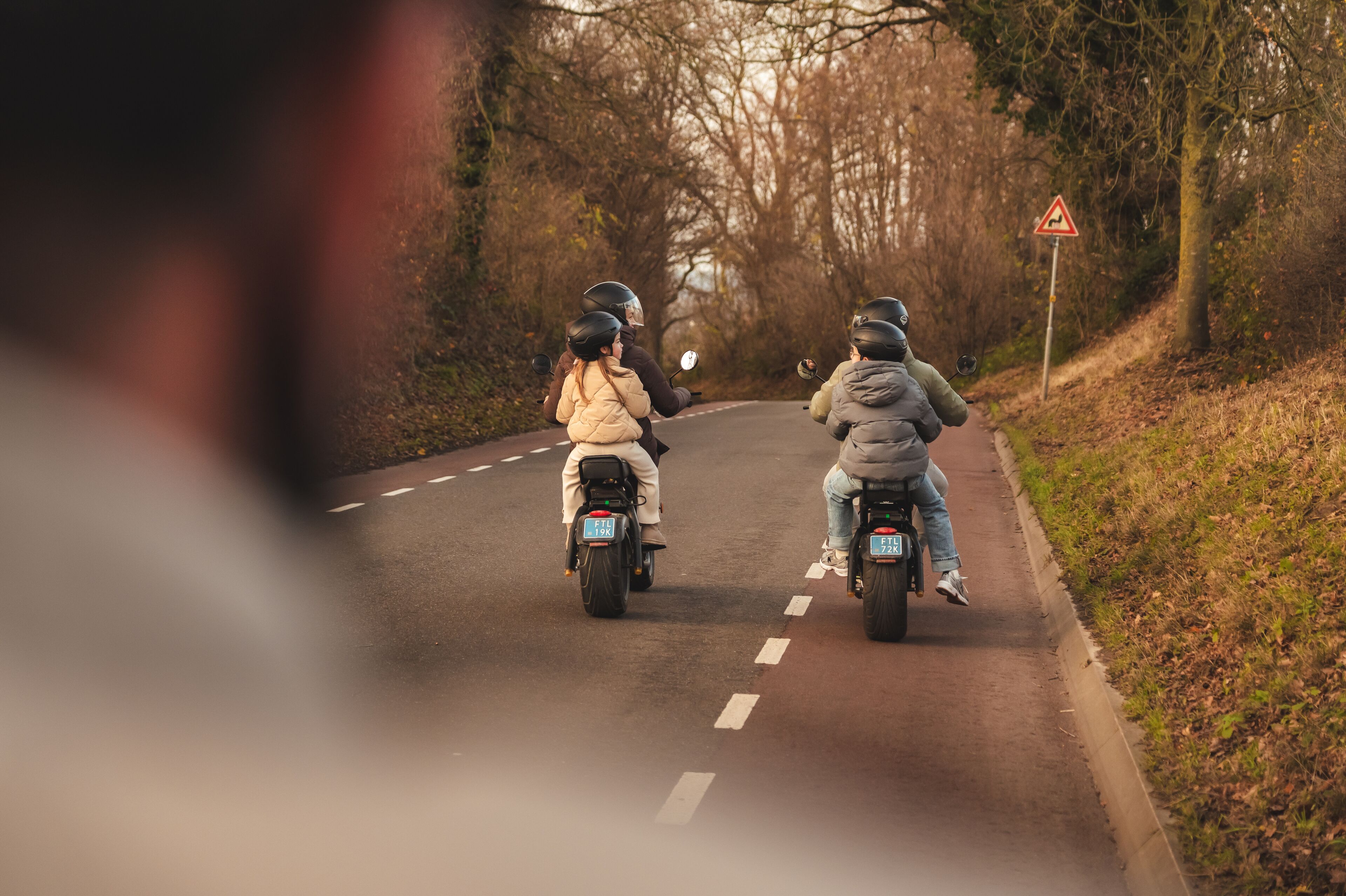 Deux motocyclistes sur une route où est placé un panneau d’avertissement triangulaire.