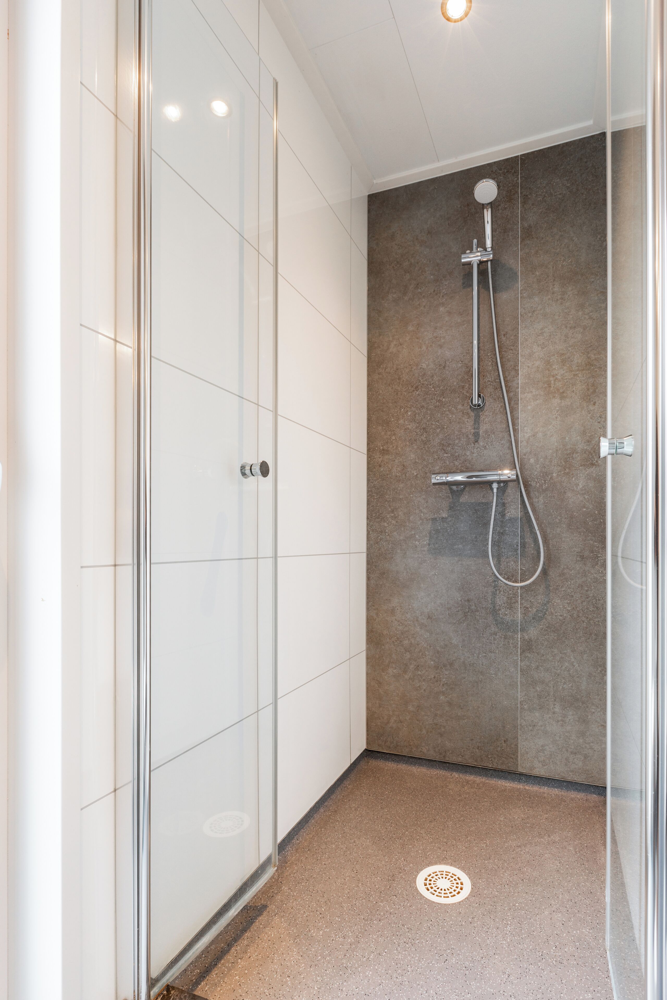 A modern bathroom with a glass shower enclosure, a wall-mounted showerhead, and a floor drain.