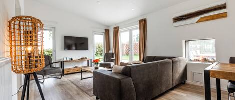 A modern living room with a grey sofa, a wooden dining table, and a TV mounted on the wall.