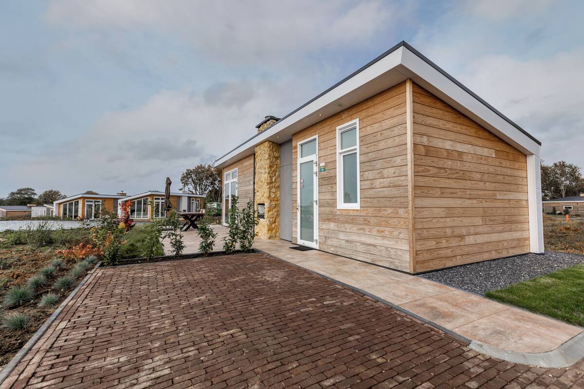 A modern single-story building with a wooden exterior, a brick pathway leading to the entrance, and a small garden area.
