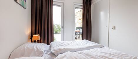 A hotel room with two beds, a lamp, and a view of the outside.