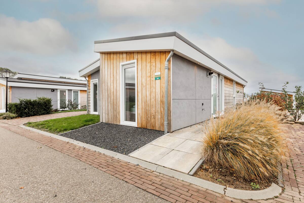 A modern building with a wooden facade, a door, and a small garden area with grass and plants.