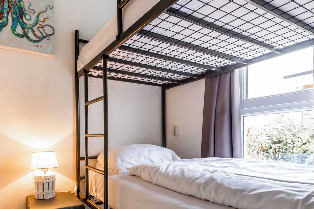 A bunk bed room with a window, a bedside lamp, and a painting on the wall.
