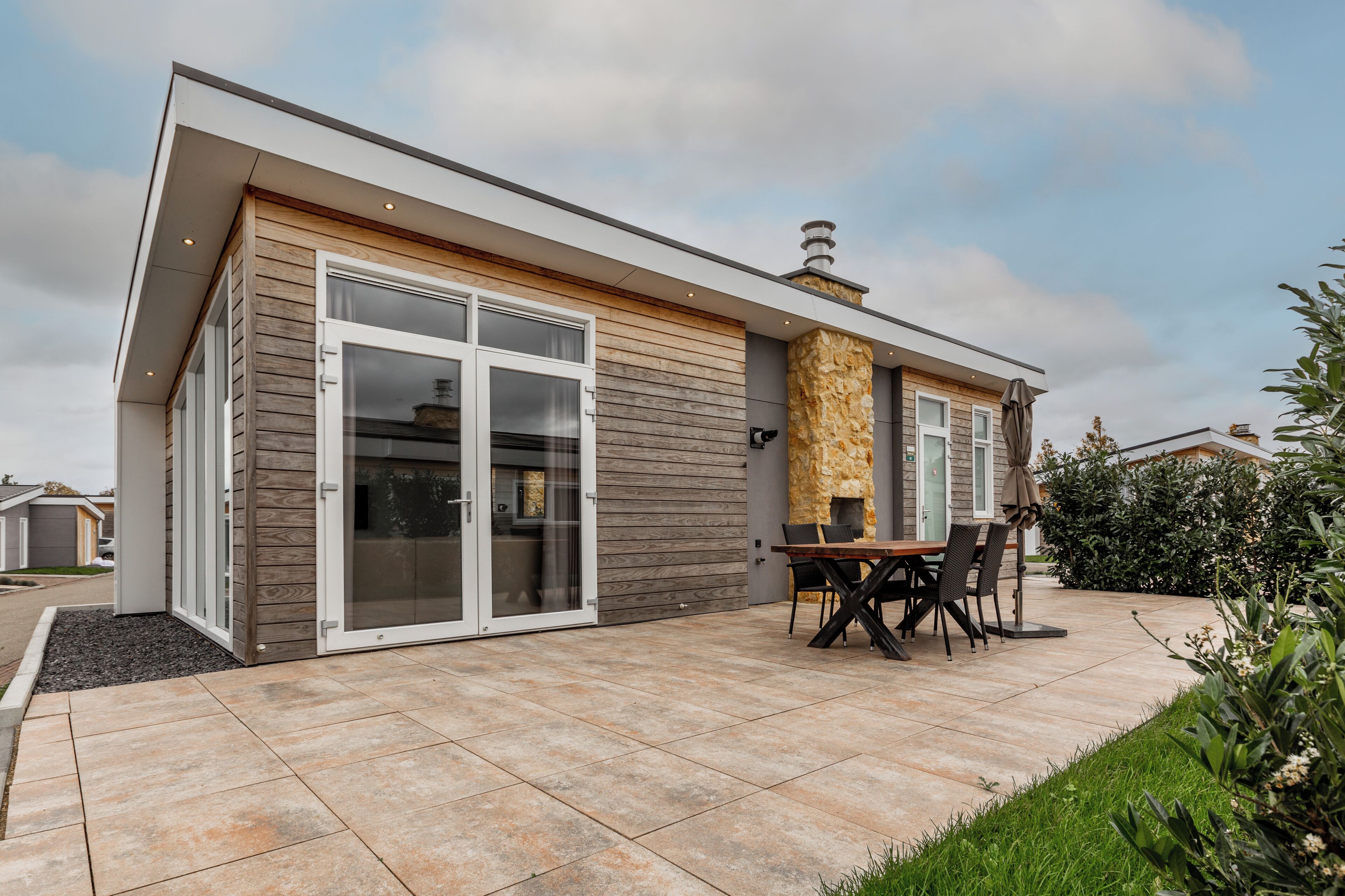 A modern house with a large sliding glass door, a stone fireplace, and a patio with outdoor furniture.