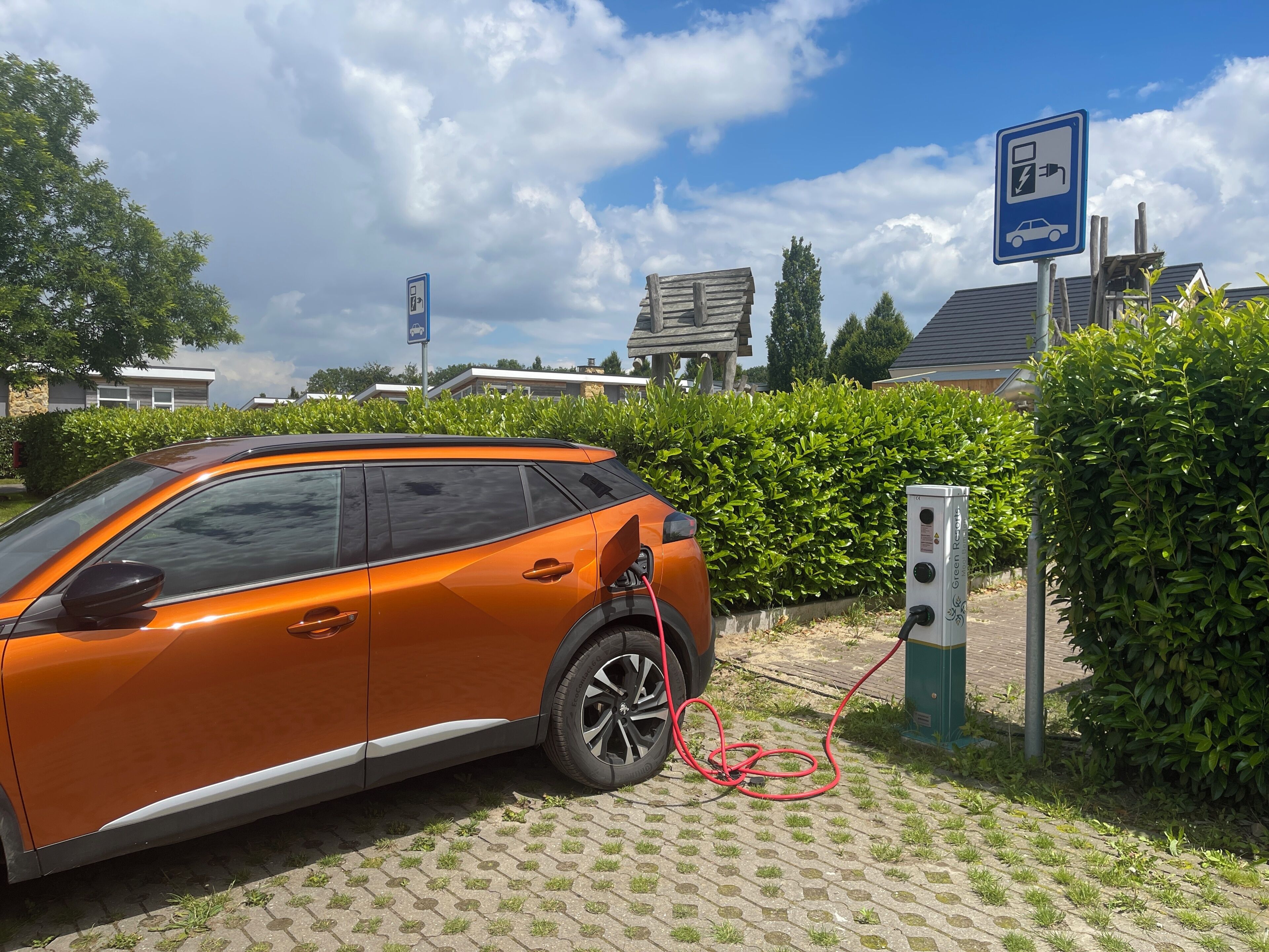 Un véhicule électrique orange est en cours de recharge à une borne dont le panneau bleu indique que la recharge est disponible.