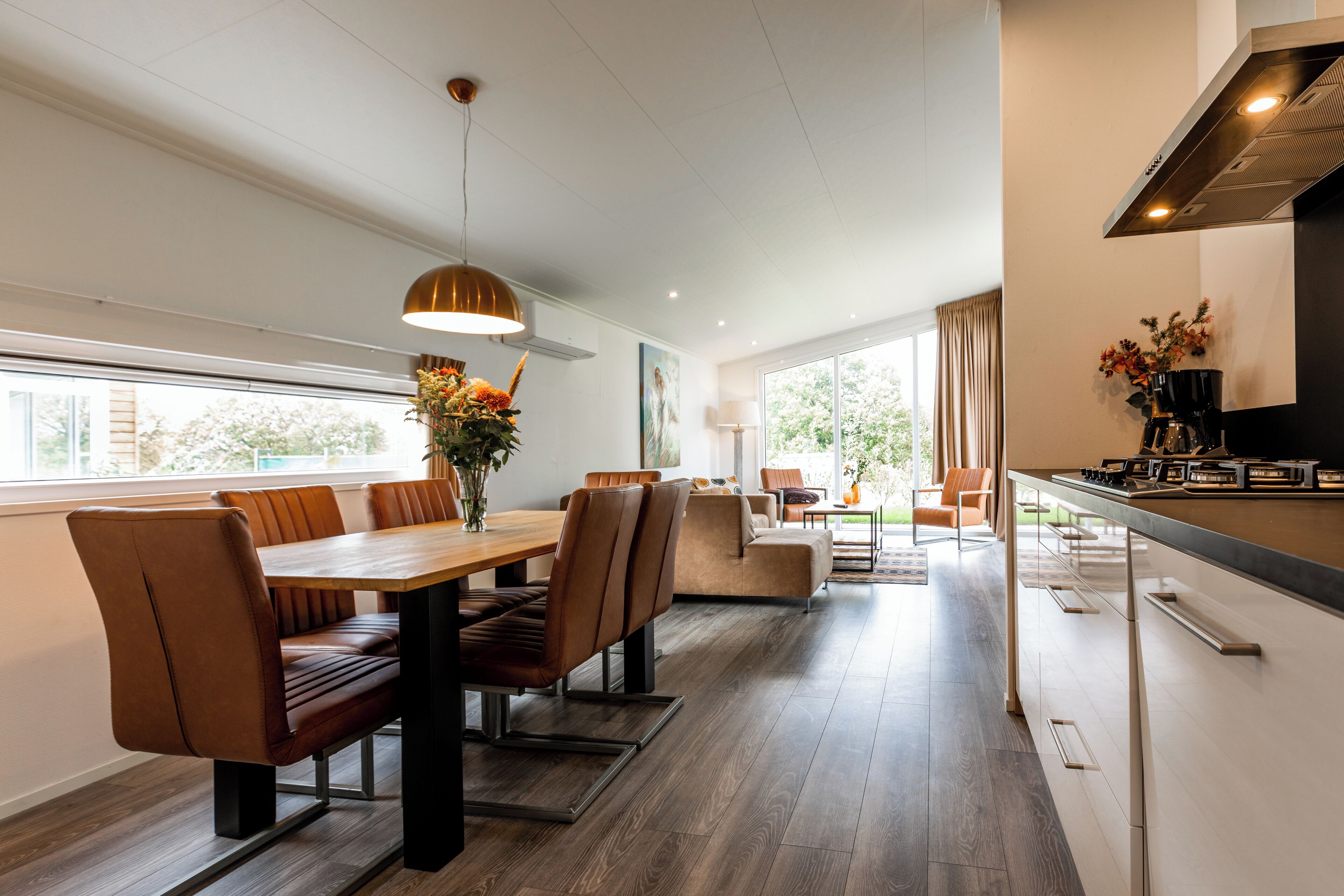 A modern kitchen with a central island, a dining area with brown leather chairs, and a large window providing natural light.