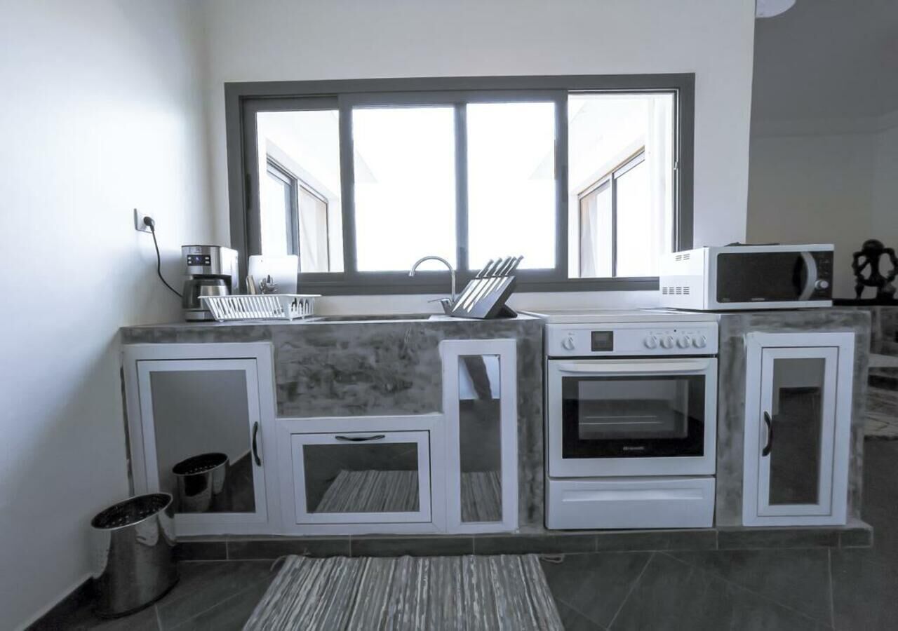 A kitchen with a built-in oven, microwave, and coffee maker. There is a window above the sink and cabinets with a tiled backsplash.