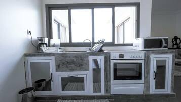 Una cocina con horno integrado, microondas y cafetera. Hay una ventana sobre el fregadero y alacenas con salpicadero de azulejos.