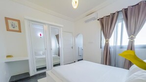 A hotel room with a bed, a wardrobe, a mirror, and a window with curtains. - Kapinga's house (Mbour)
