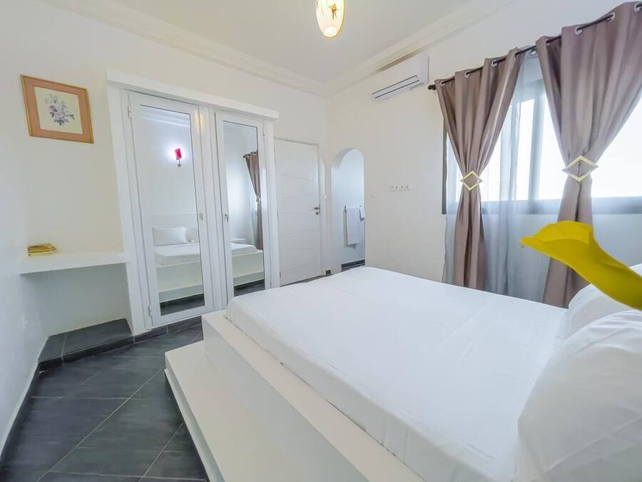 Una habitación de hotel con cama, armario, espejo y ventana con cortinas.