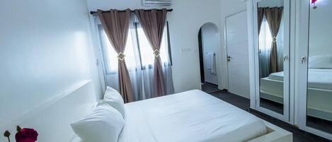 Quarto com cama, cortinas, espelho e guarda-roupa.