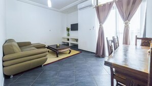 A modern living room with a sofa, a coffee table, a dining table, and a TV mounted on the wall. - Kapinga's house (Mbour)