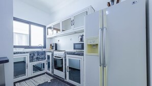A modern kitchen with white cabinets, a built-in oven, a microwave, and a refrigerator. - Kapinga's house (Mbour)