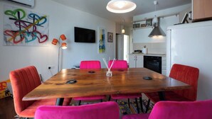 A modern kitchen with a wooden dining table, bright pink chairs, and a colorful abstract painting on the wall.