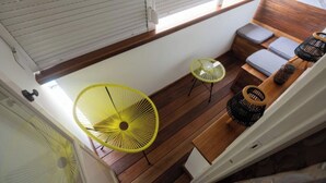 A room with wooden flooring, a yellow chair, a small table, and a bench with cushions.