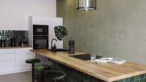 A modern kitchen with a wooden countertop, bar stools, a sink, and a large green plant.
